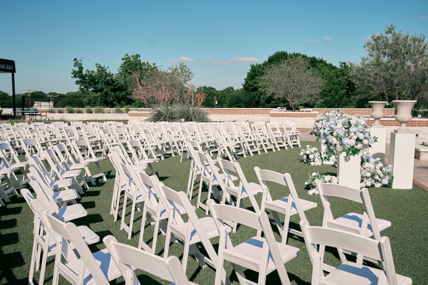 Rows of white folding chairs arranged on green lawn for an outdoor wedding ceremony with floral arrangements.