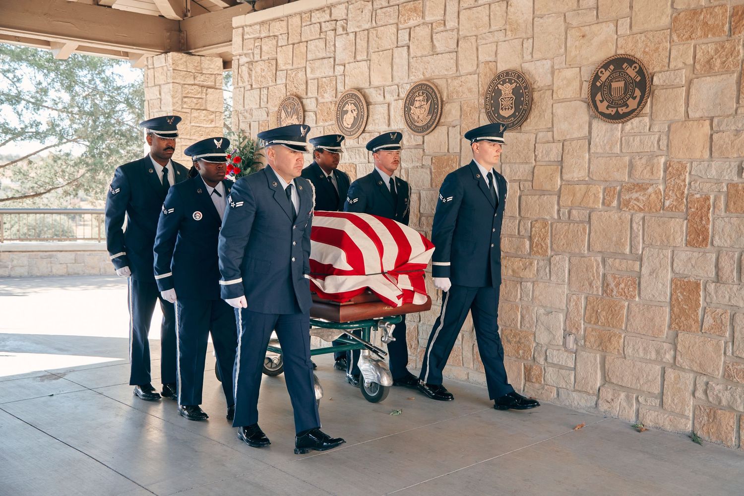 Military honor guard carrying flag-draped casket at an outdoor memorial service ceremony.