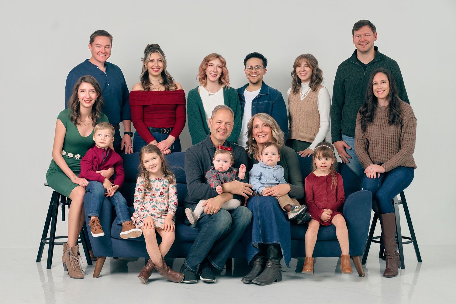 A large multigenerational family of fourteen poses together for a professional studio portrait.