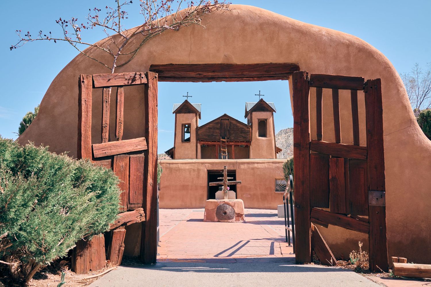 Historic adobe church with wooden gates in New Mexico, featuring twin bell towers and traditional Southwestern architecture.