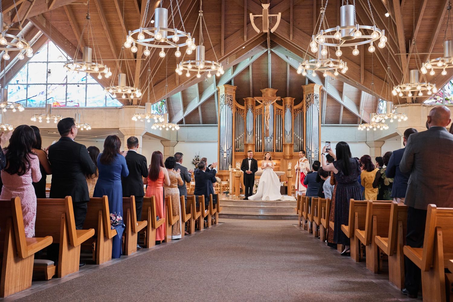 Guests stand as bride and groom exchange vows at church altar during elegant wedding ceremony.