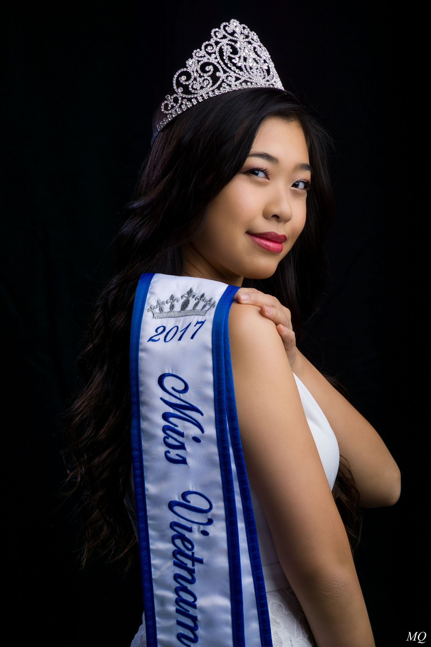 Young woman wearing a 2017 Miss Vietnam pageant sash and tiara in a white gown poses for a portrait.