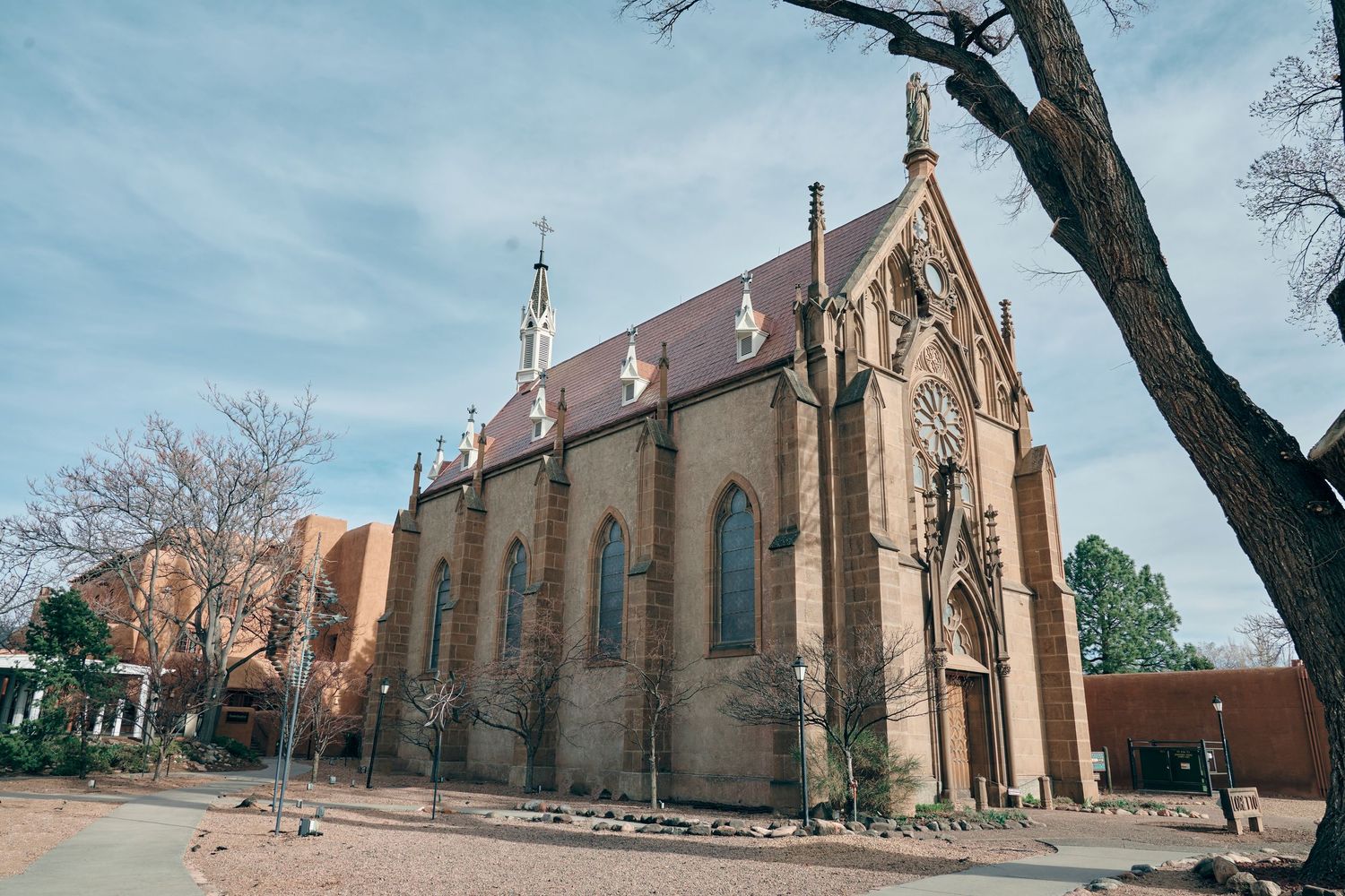 Historic Gothic stone chapel with arched windows and spire under blue sky in Santa Fe, New Mexico.