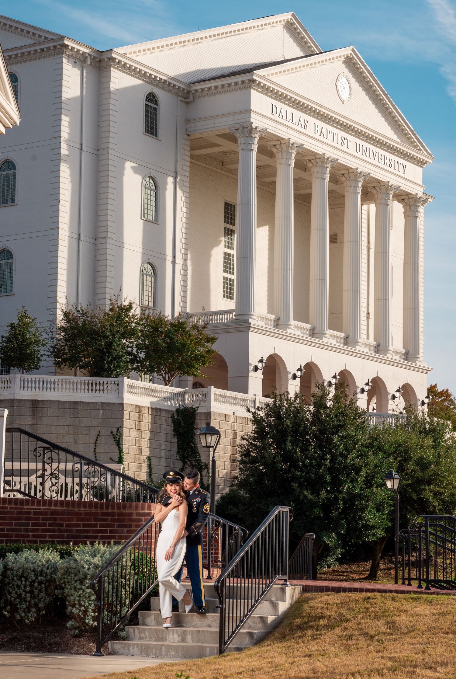 Couple posing on steps of Dallas Baptist University building in wedding attire.