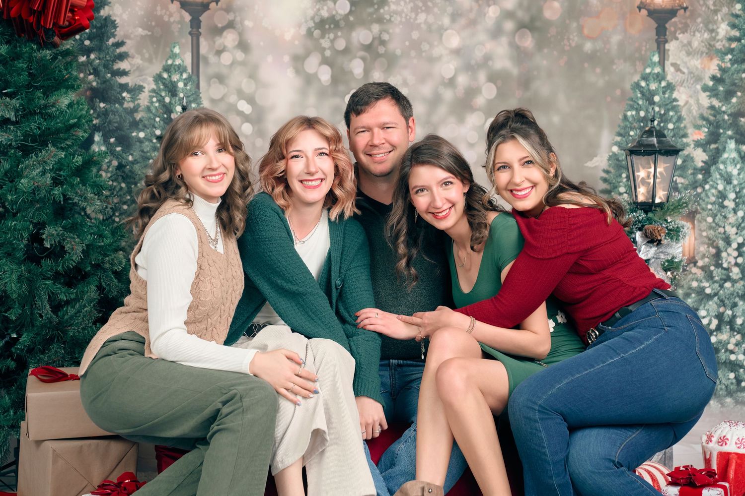A festive group of five adults poses together smiling near decorated Christmas trees in a holiday portrait.
