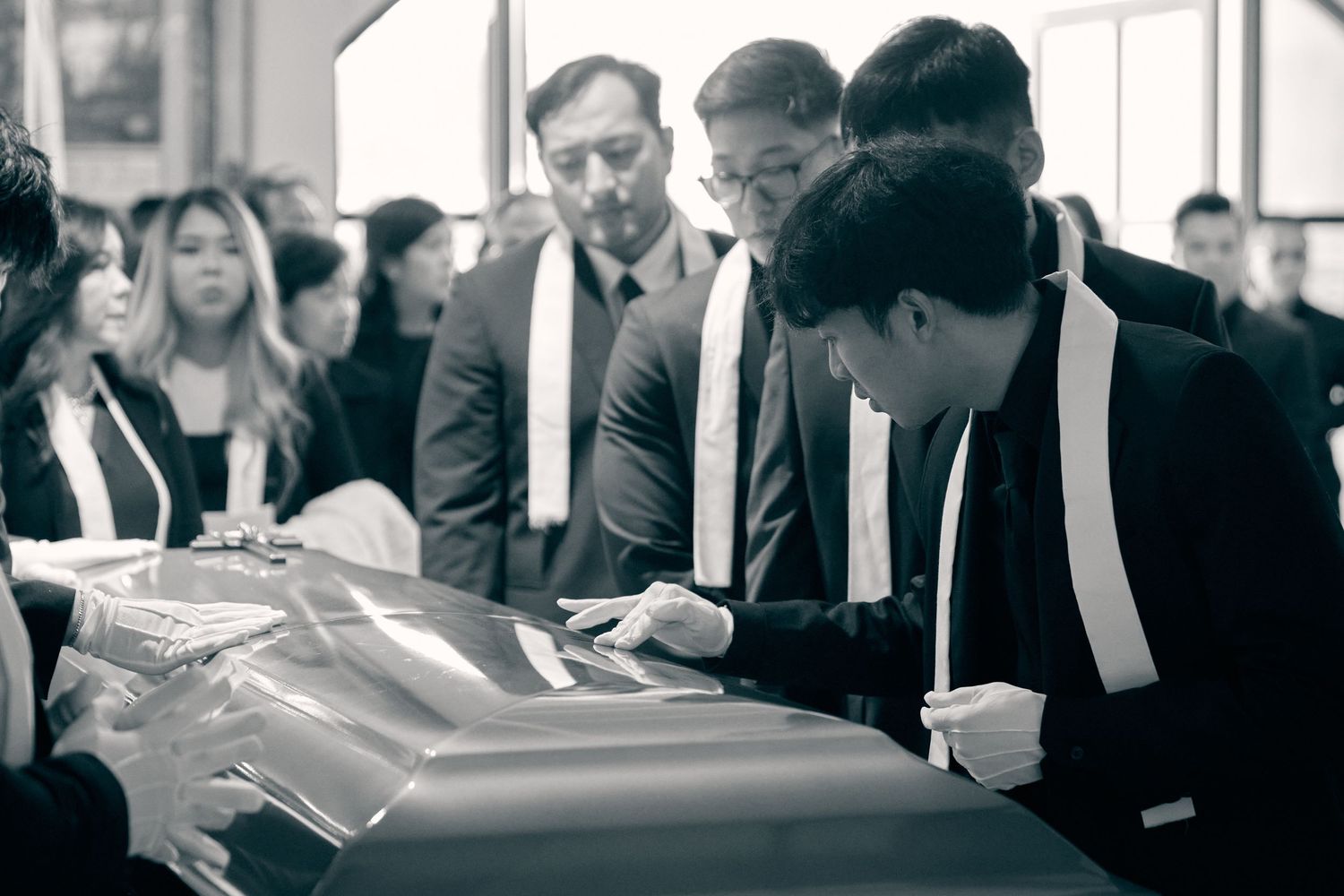 Black and white photo of mourners gathered around a casket during a funeral service.
