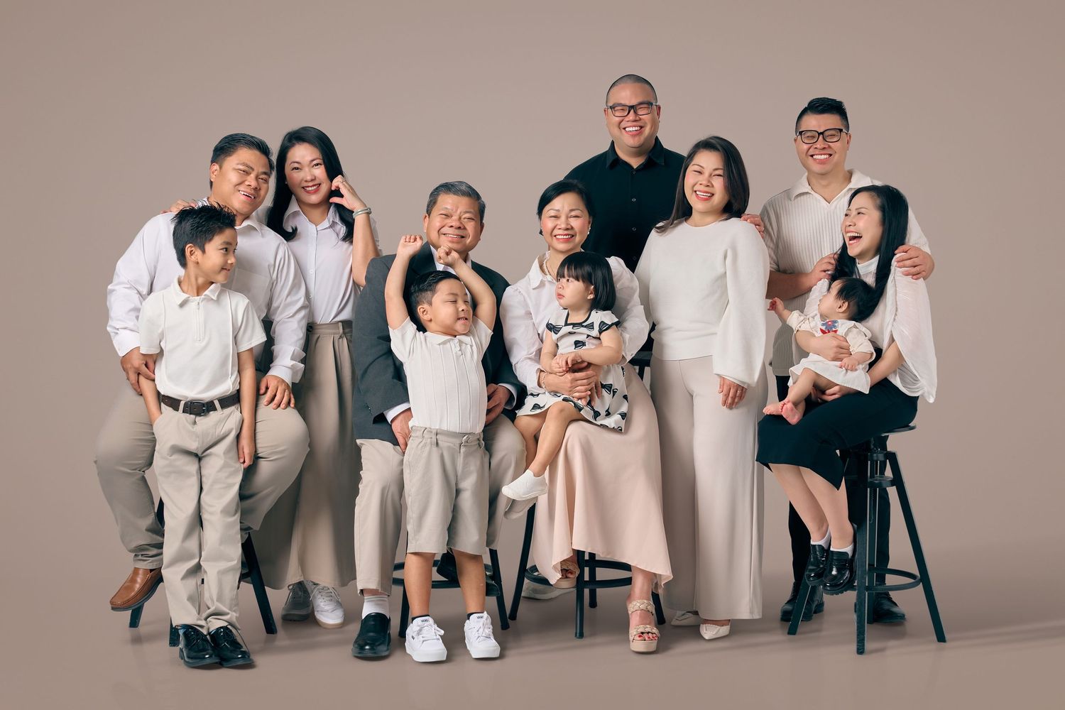 Extended Asian family studio portrait with grandparents, parents, and children in neutral coordinated outfits.