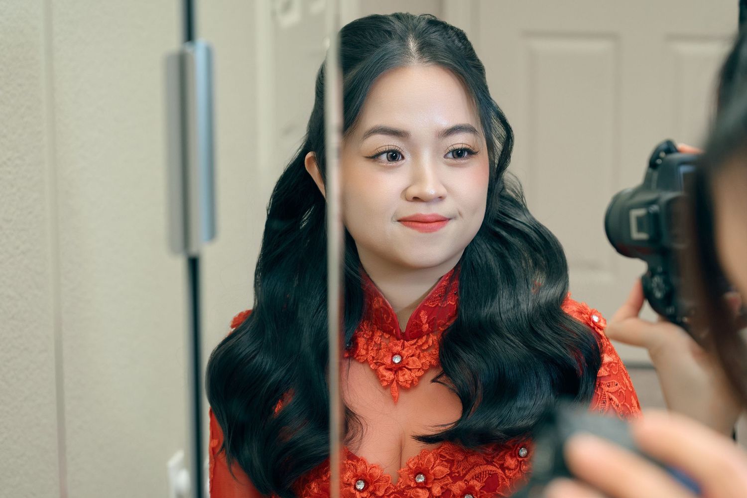 Young woman in red ao dai traditional Vietnamese dress smiling while being photographed.