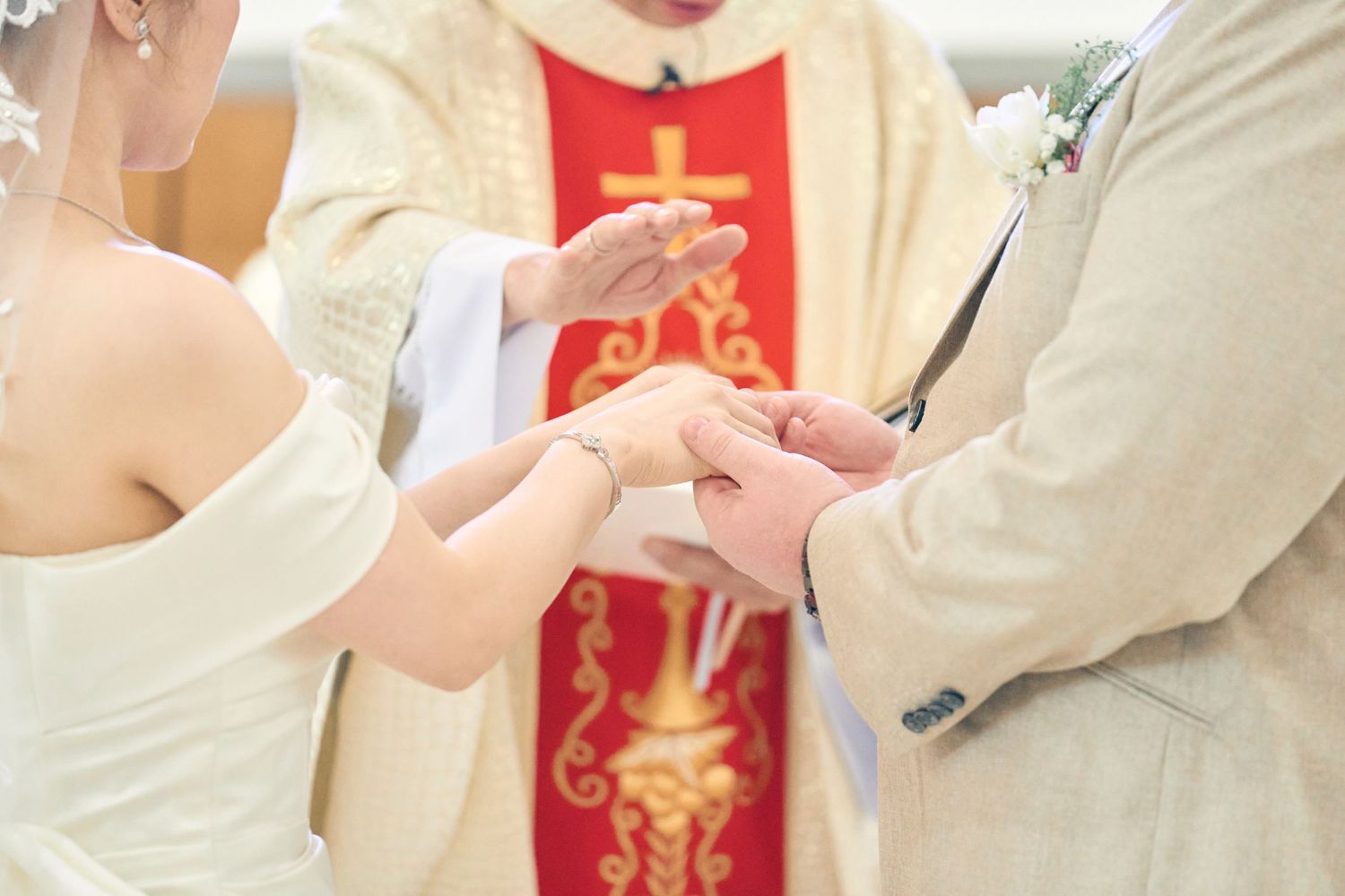 Priest officiating ring exchange ceremony between bride and groom at a Catholic wedding.