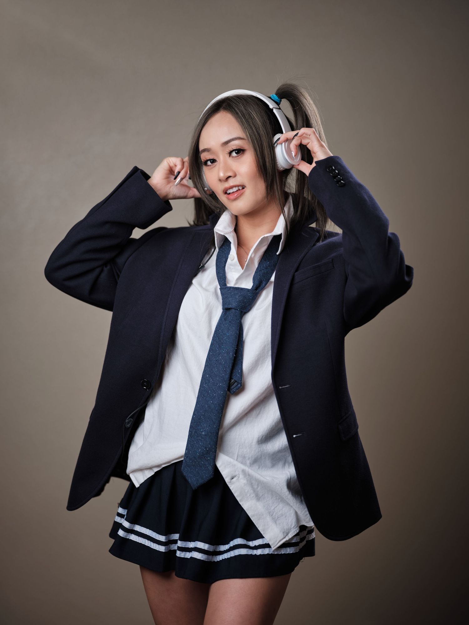 Young Asian woman in school uniform cosplay holding headphones in studio portrait.