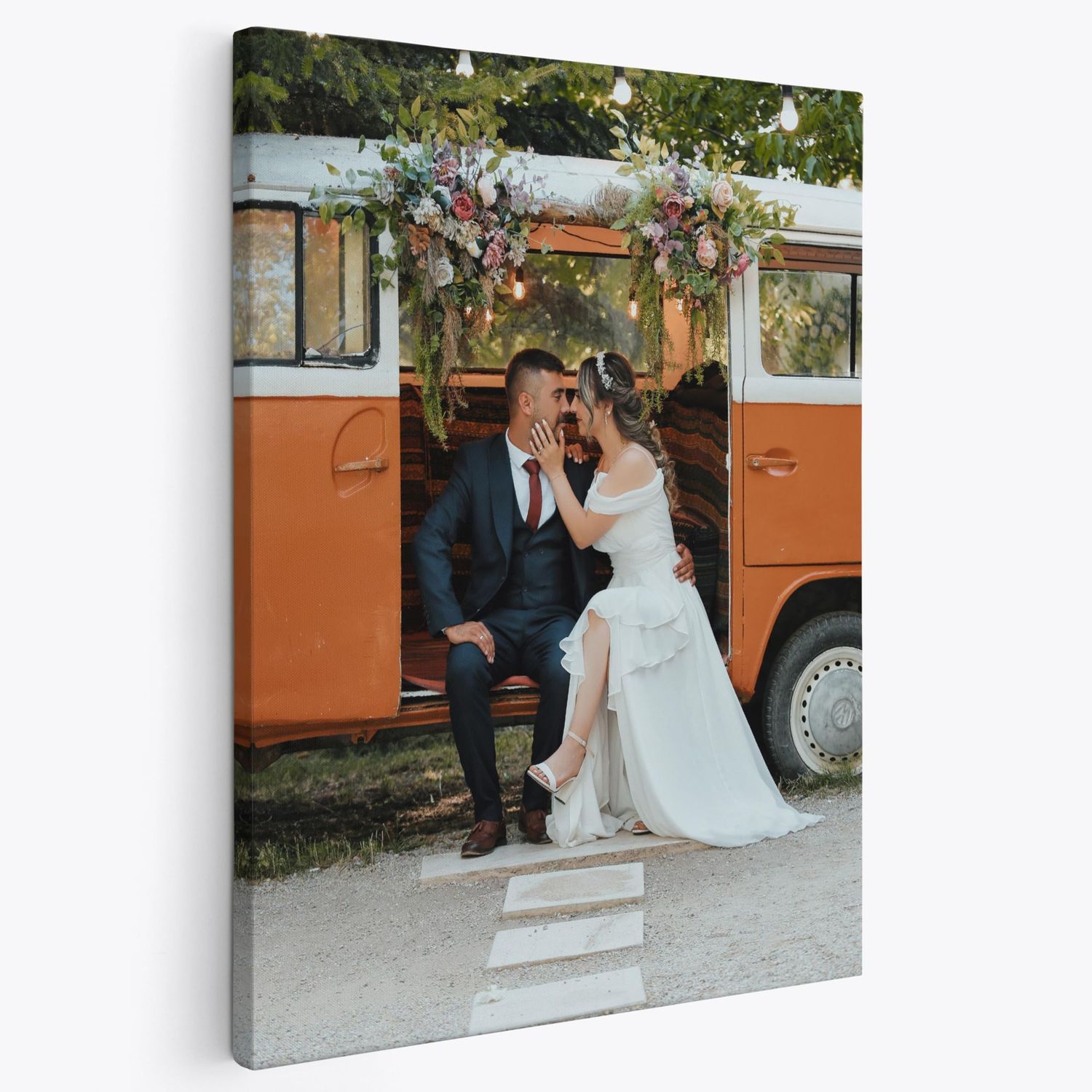 A canvas print of a wedding couple kissing in front of a vintage orange bus decorated with flowers.