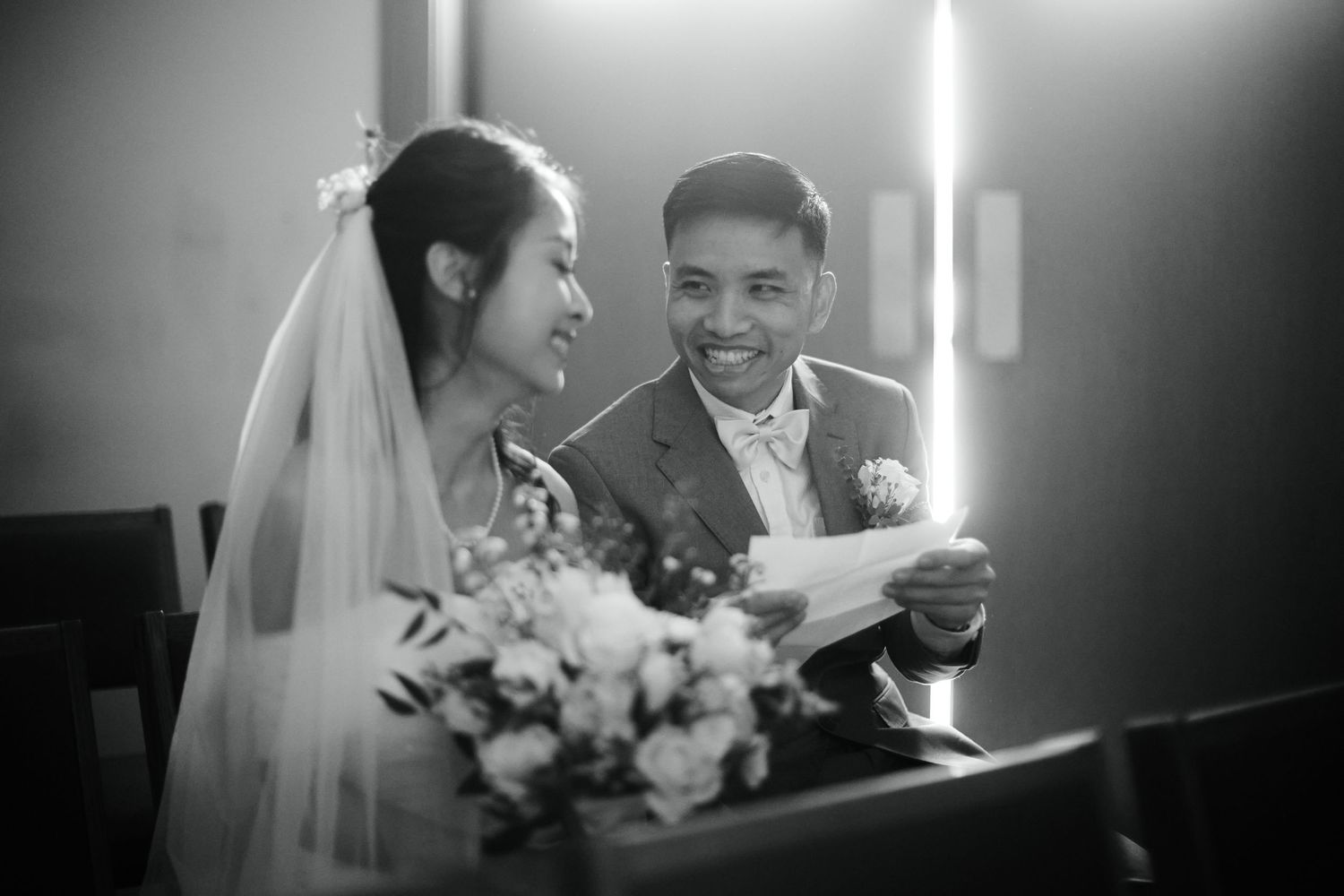 Black and white photo of a smiling bride and groom reading vows together at their wedding ceremony.