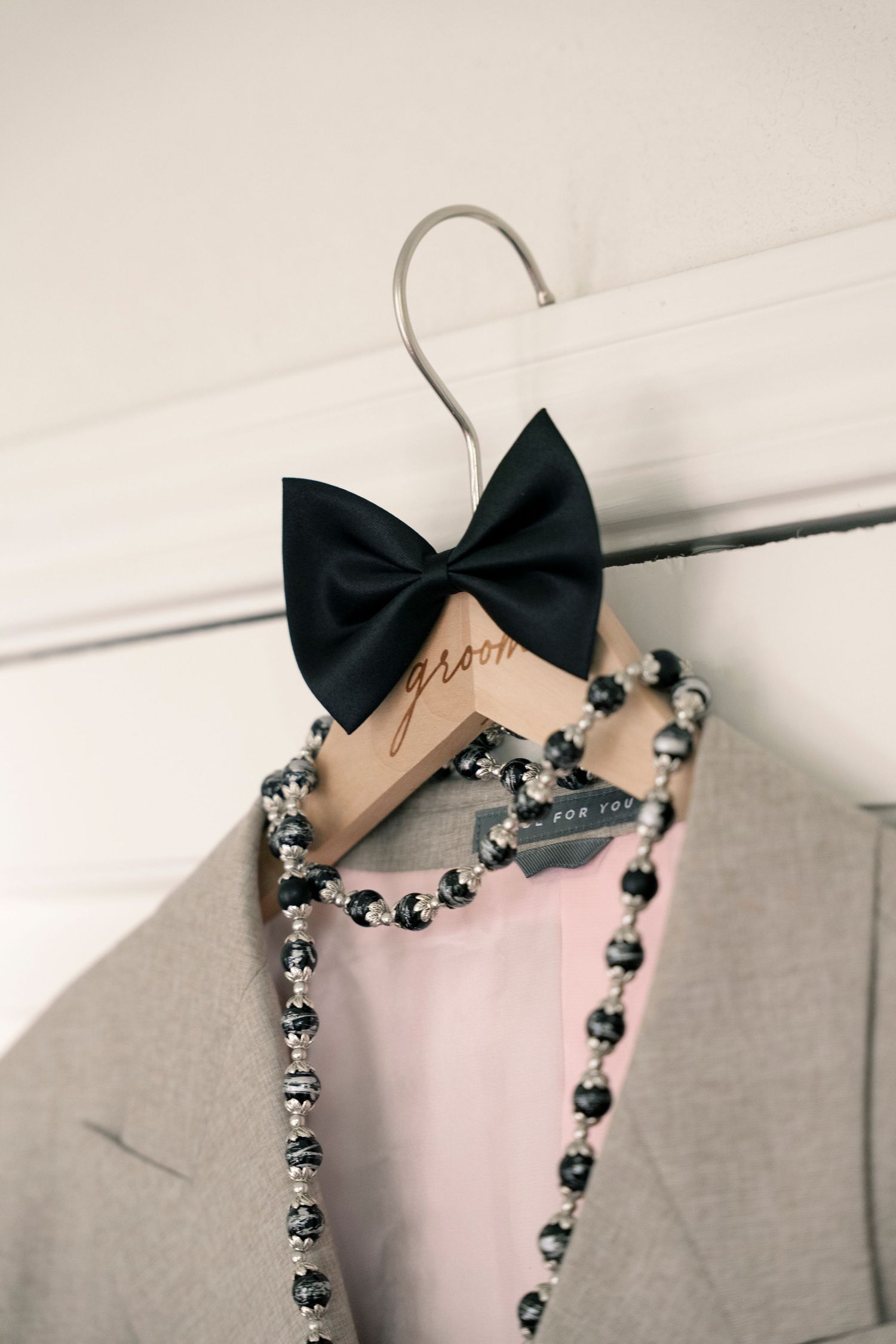 Grooms custom wooden hanger with black bow tie and beaded necklace hanging on wedding suit.