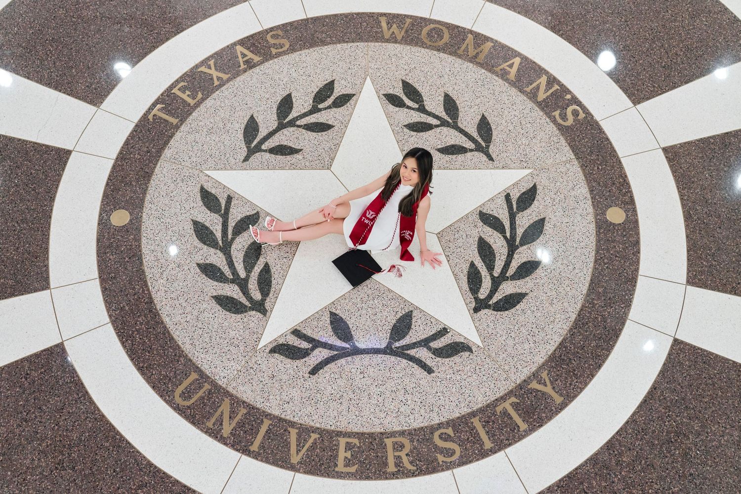 Graduate poses on Texas Woman's University seal mosaic floor from above.