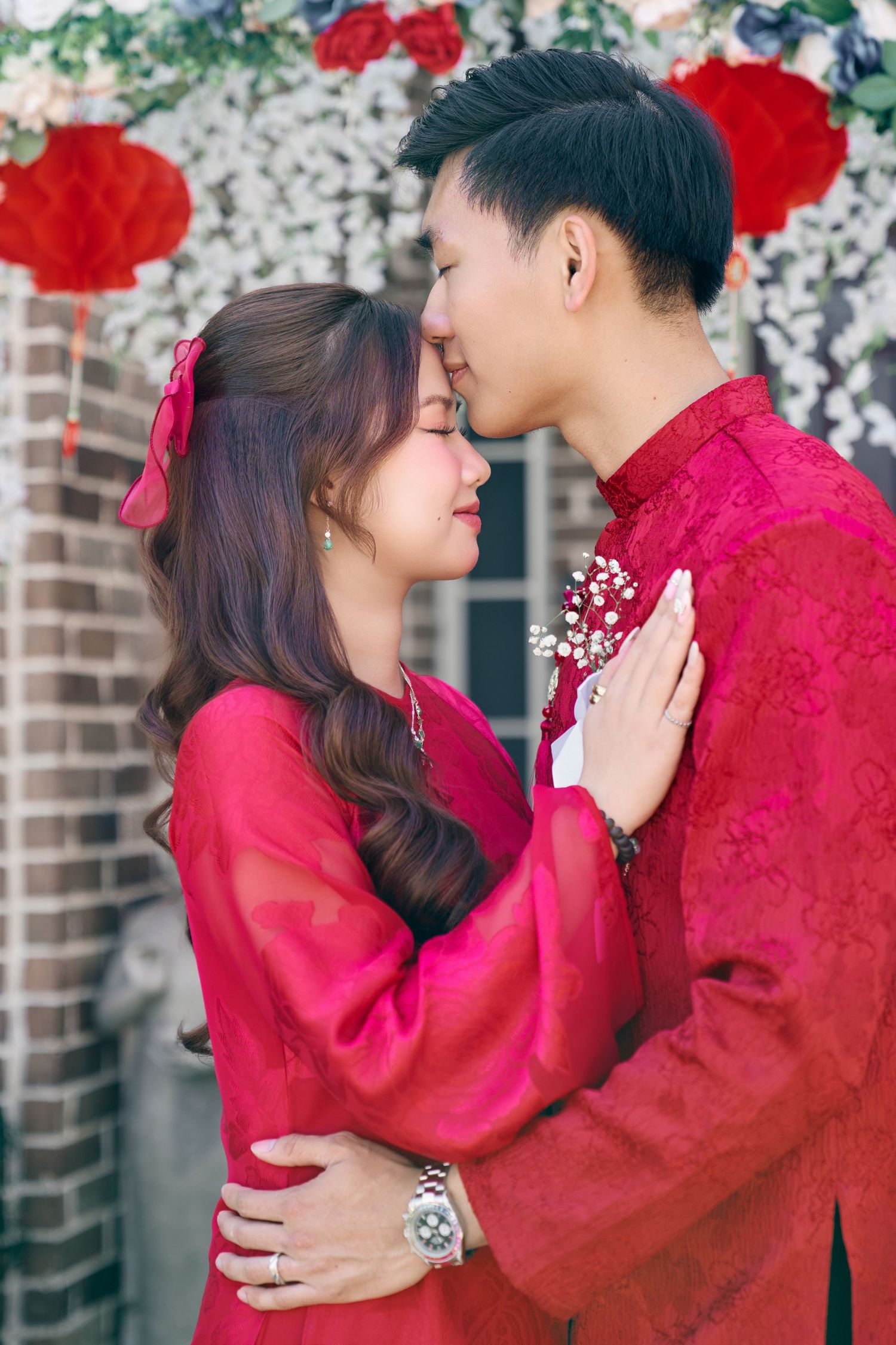 Couple in matching red traditional Chinese outfits sharing a romantic moment with foreheads touching.