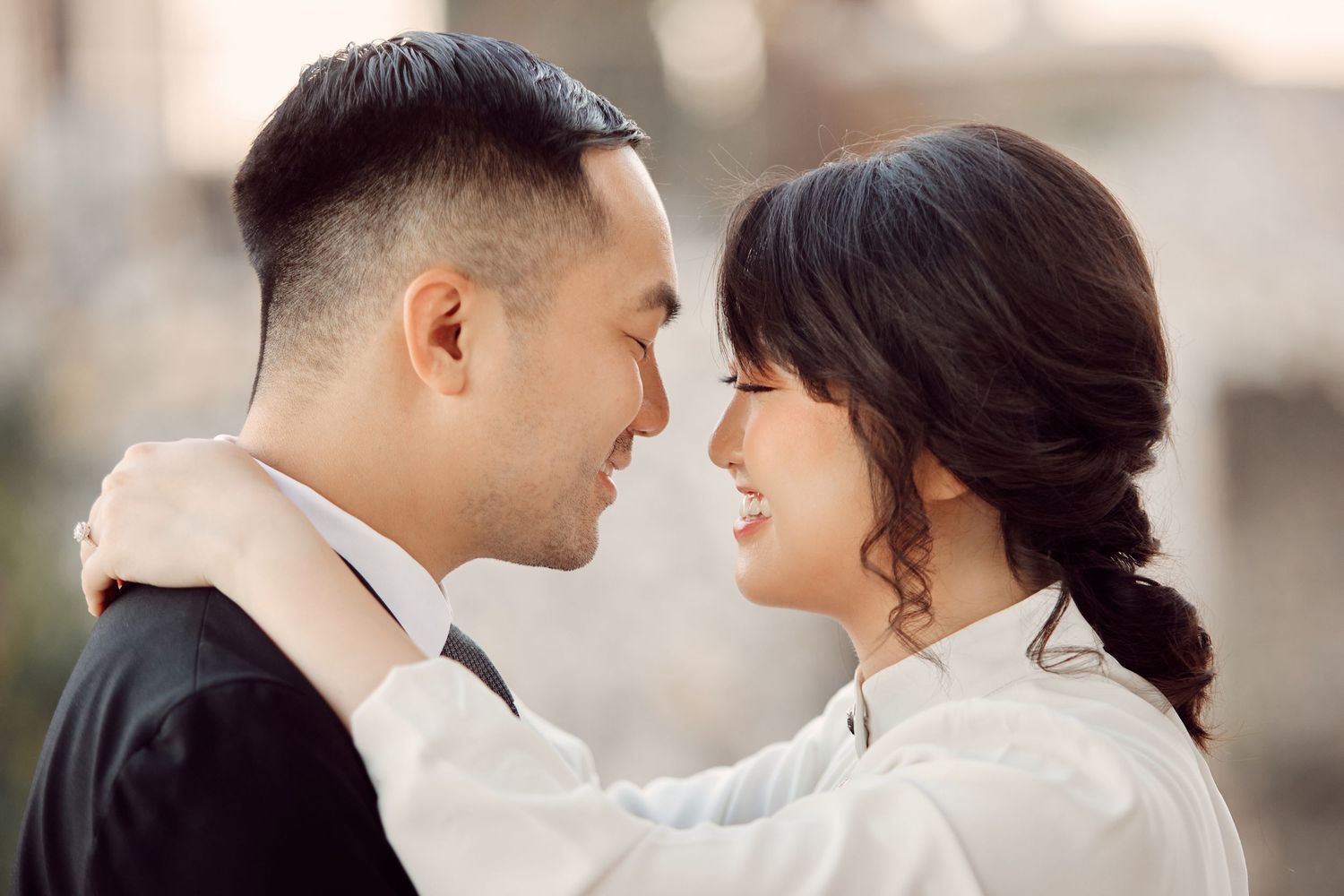 Close-up of Asian couple in formal wear smiling at each other during romantic outdoor photo session.