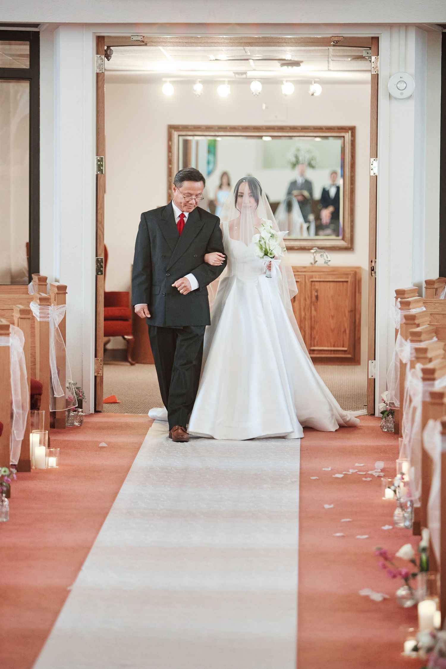 Father walks bride down the aisle in a candlelit church wedding ceremony.