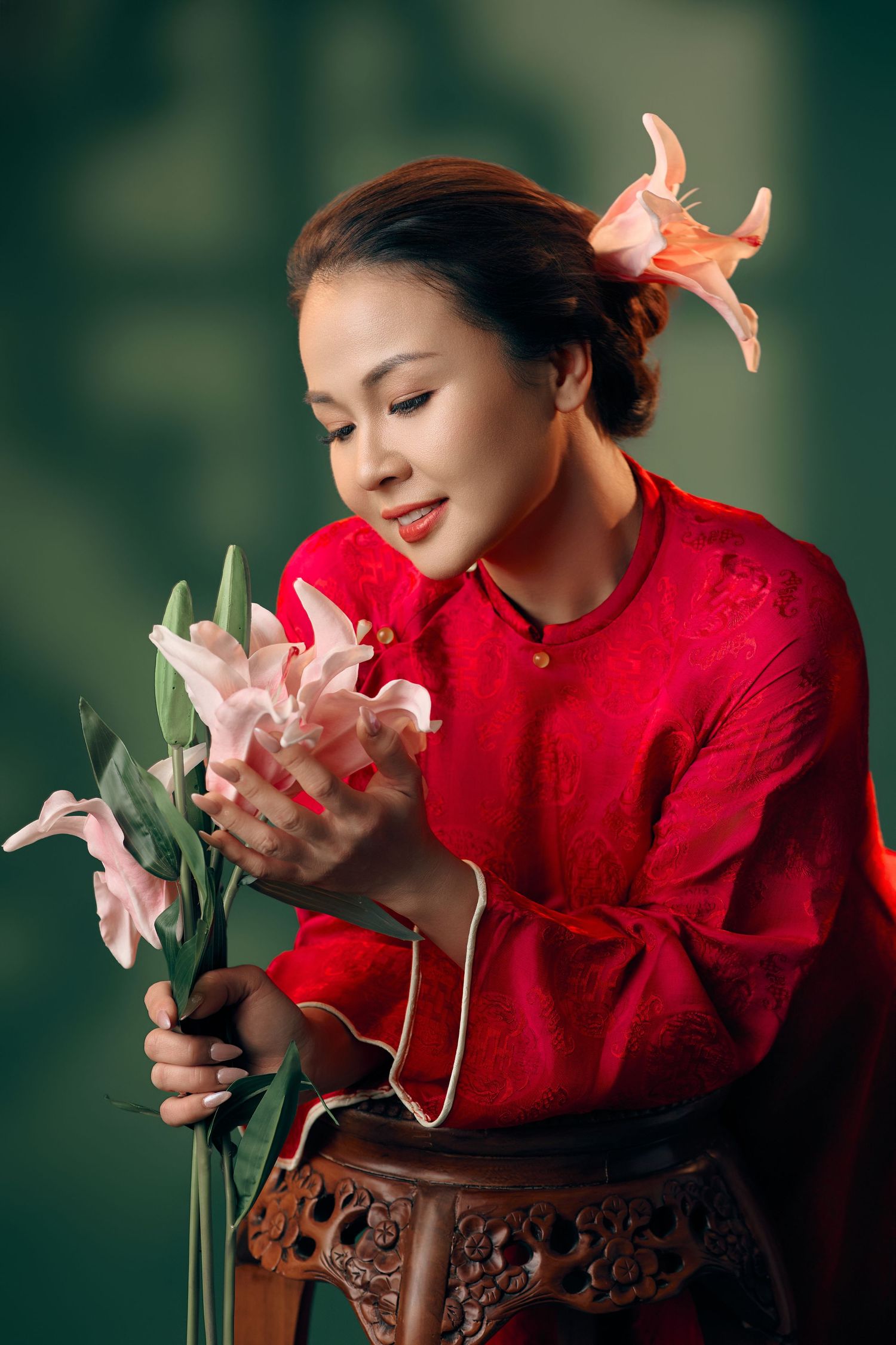 Woman in red traditional Asian dress holding pink lily flowers with a flower in her hair.