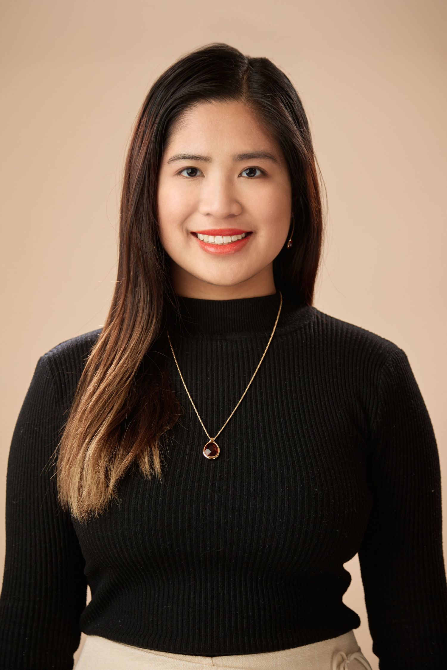 Cheerful young Asian woman in black turtleneck with necklace on beige background.