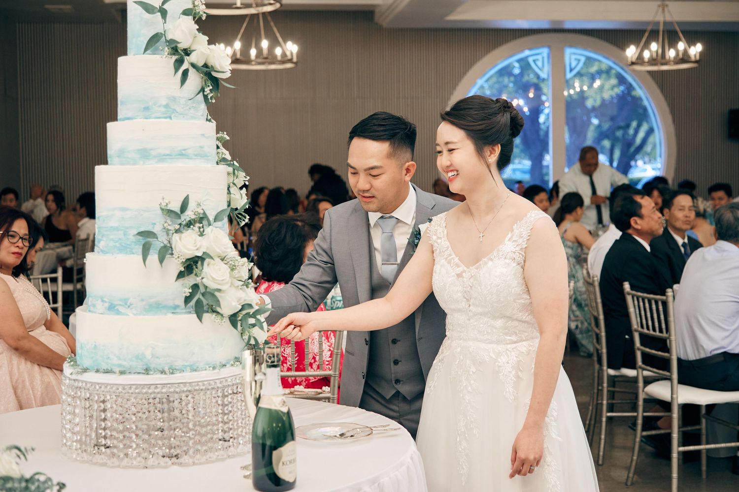 Smiling bride and groom cut their elegant multi-tiered white wedding cake at reception.