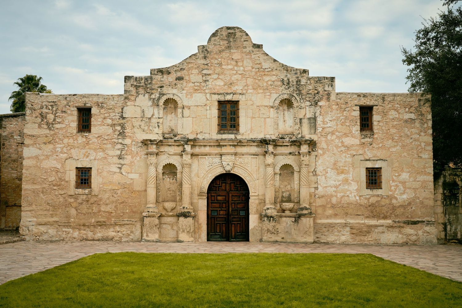 Historic Alamo mission facade in San Antonio, Texas, featuring limestone walls and ornate wooden doors.