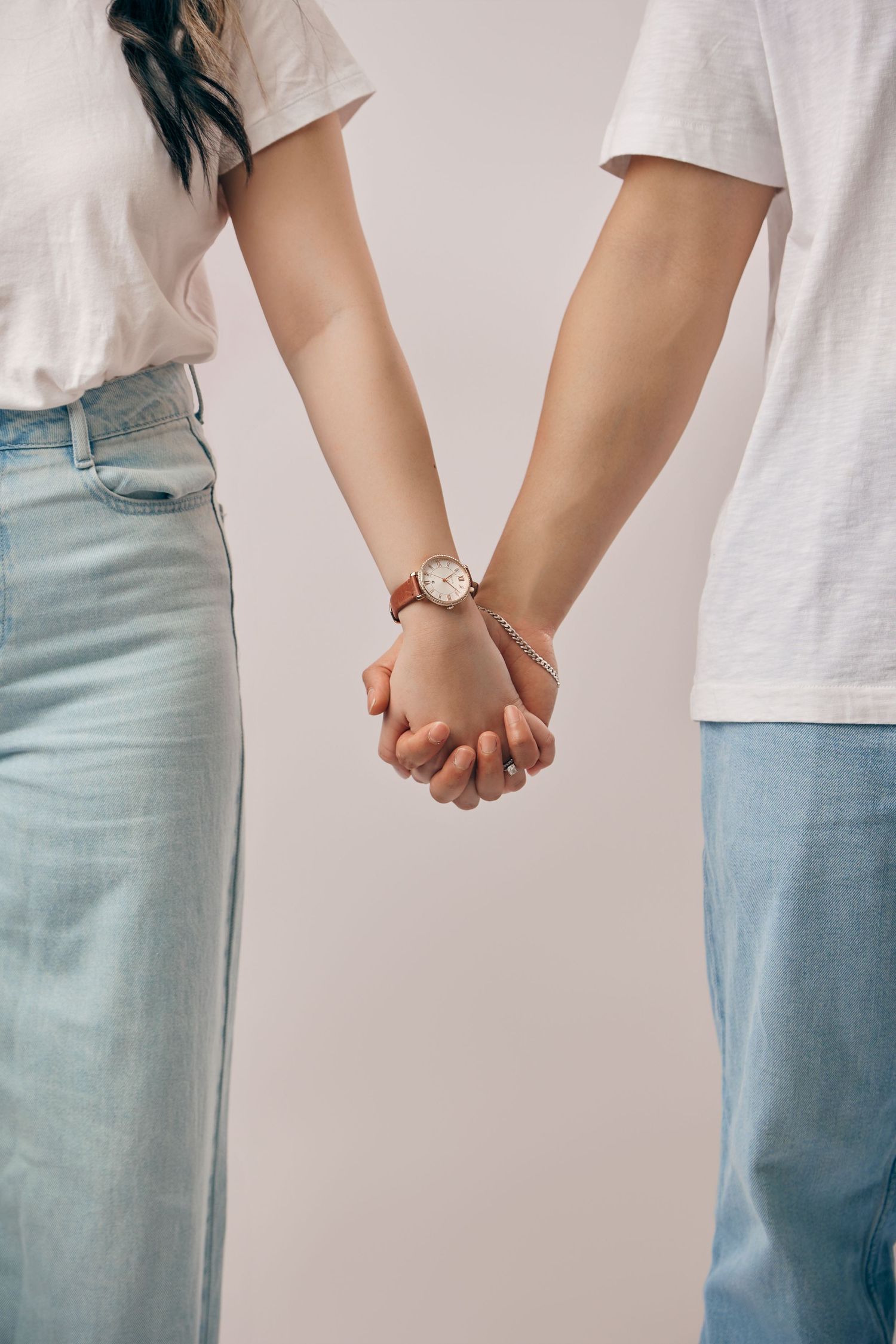 Close-up of a couple holding hands, woman wearing a leather-strap watch, in casual attire.