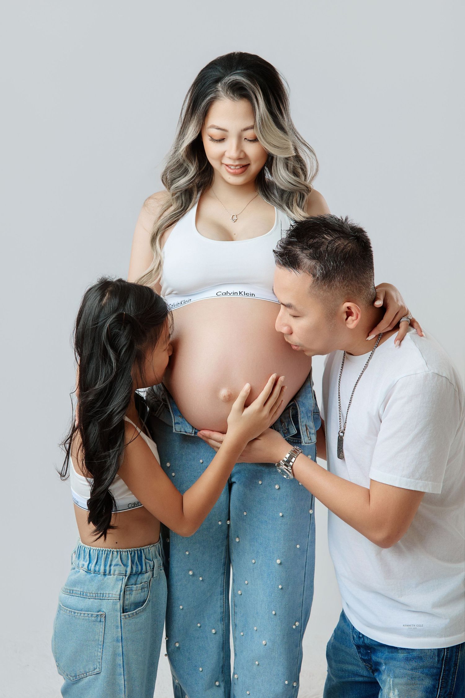 Family maternity photo with pregnant woman in white top and jeans with husband and daughter.