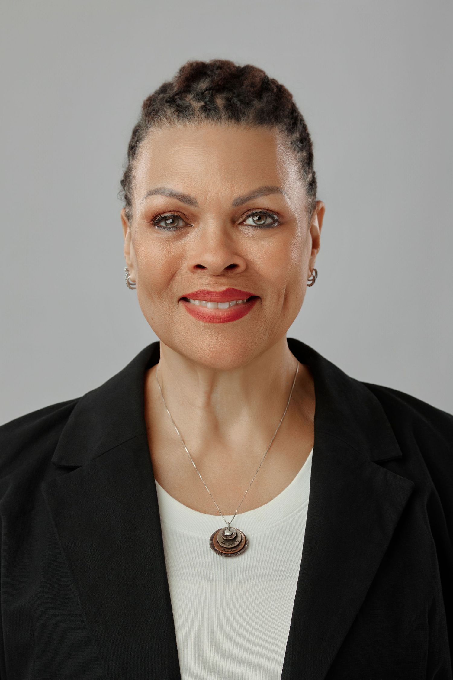 Professional headshot of a smiling middle-aged woman in a black blazer with braided updo hairstyle.