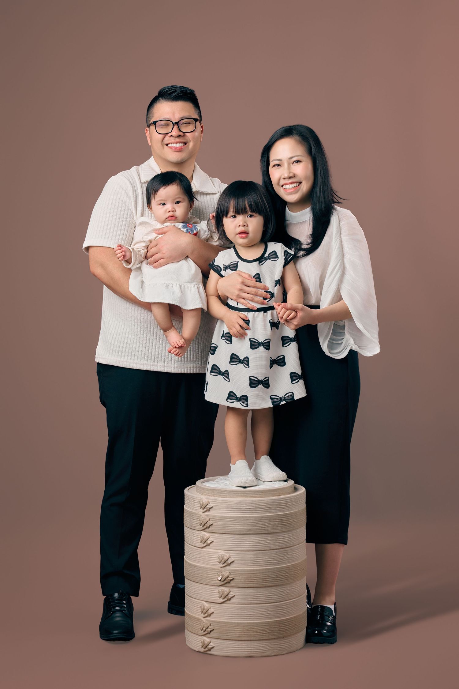 Asian family of four with two young daughters, parents in coordinated black and white outfits, studio portrait.