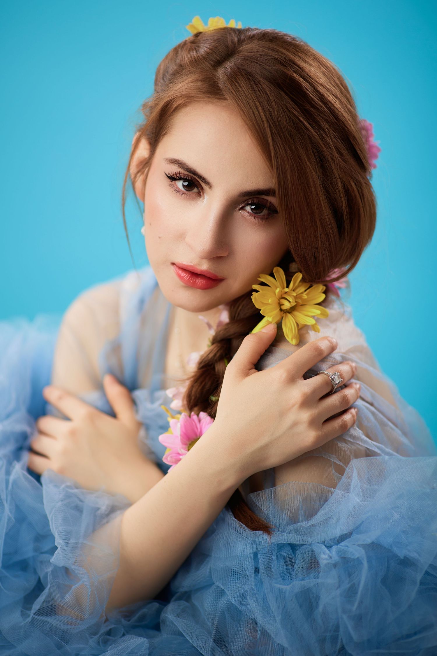 Beautiful young woman in blue tulle dress holds yellow flower with blooms in her braided hair.