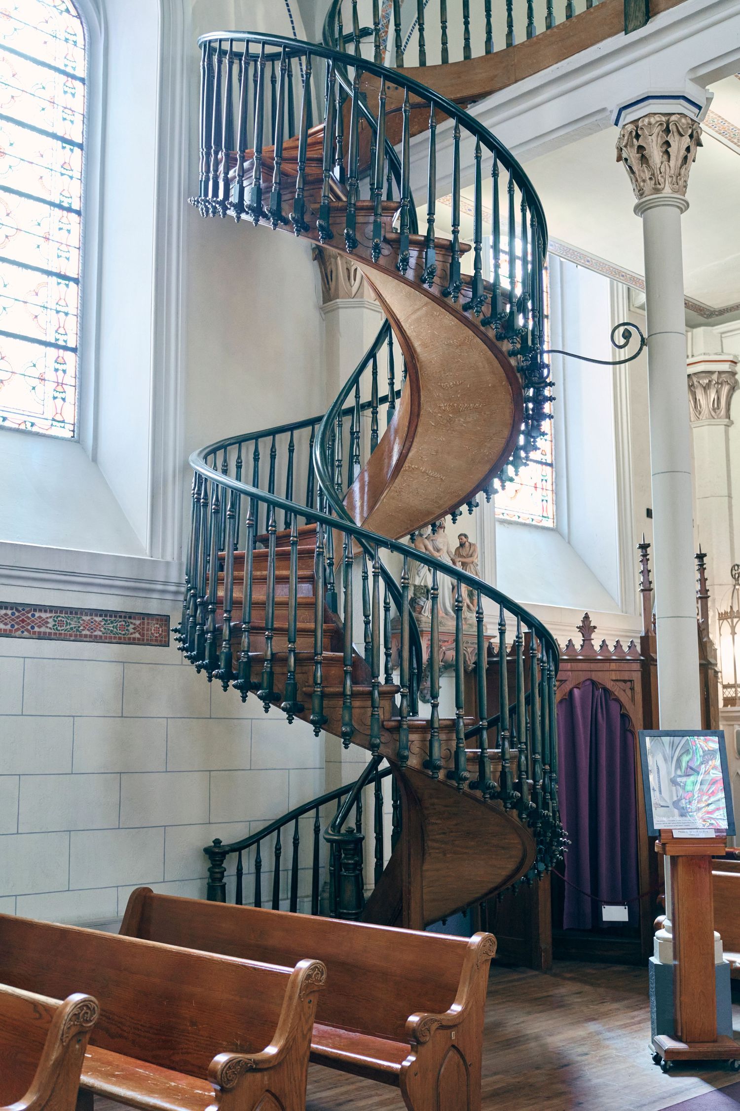 Elegant spiral staircase with green iron railings and wooden steps inside a historic chapel.