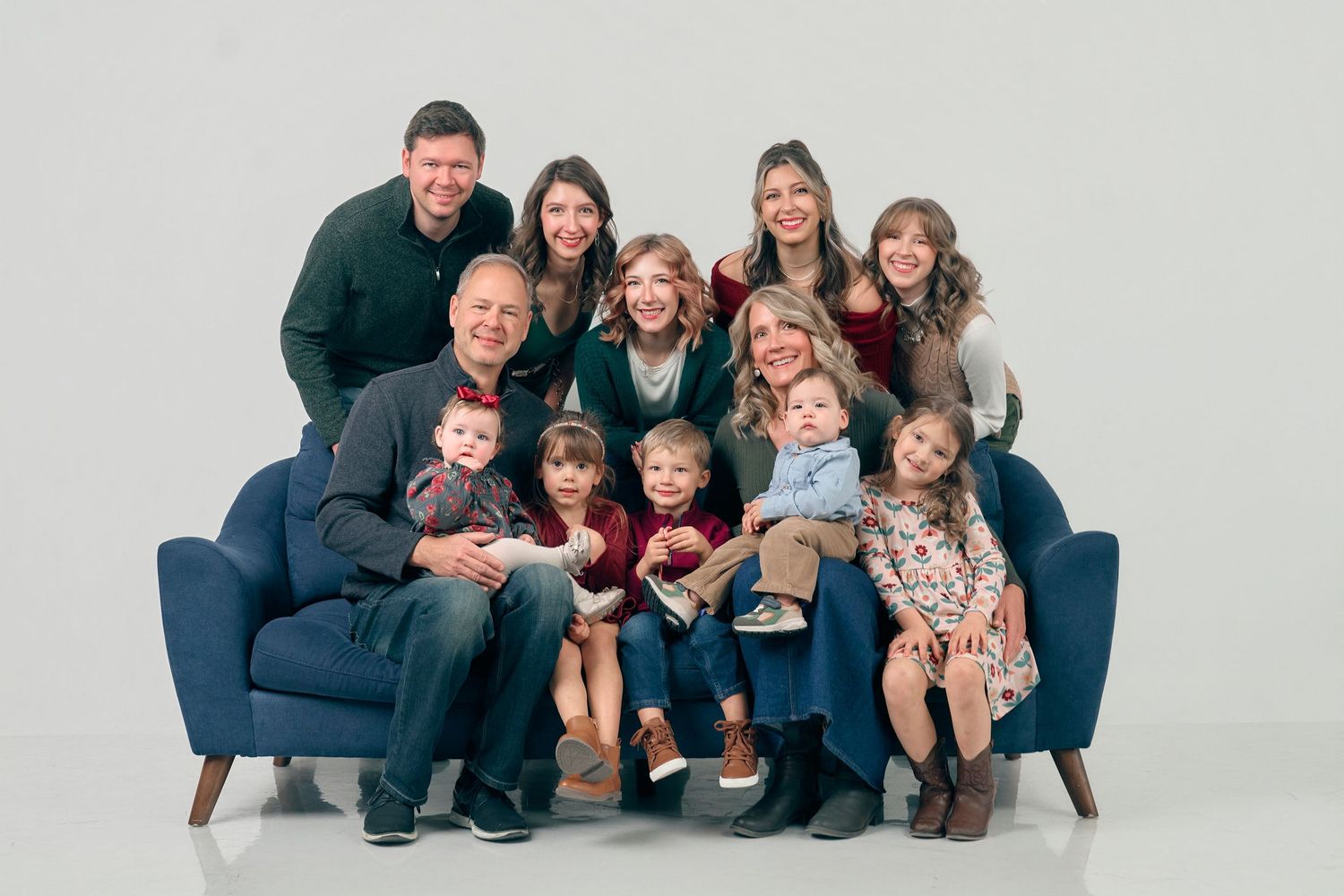 Large family portrait with grandparents, parents, and children posing together on a blue sofa against white background.