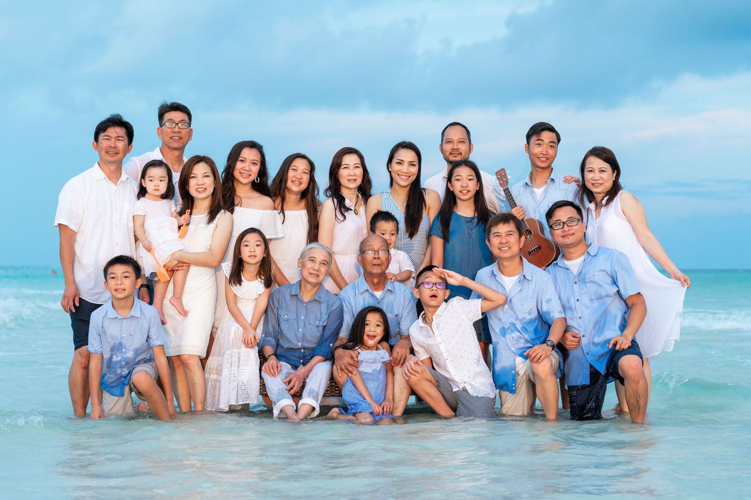 Large extended Asian family group photo on a tropical beach with turquoise ocean water in the background.