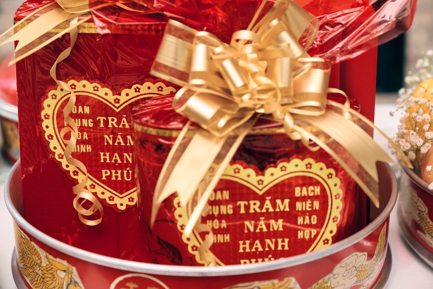 Red Vietnamese gift boxes with gold heart decorations and bow, featuring traditional wedding blessings calligraphy.