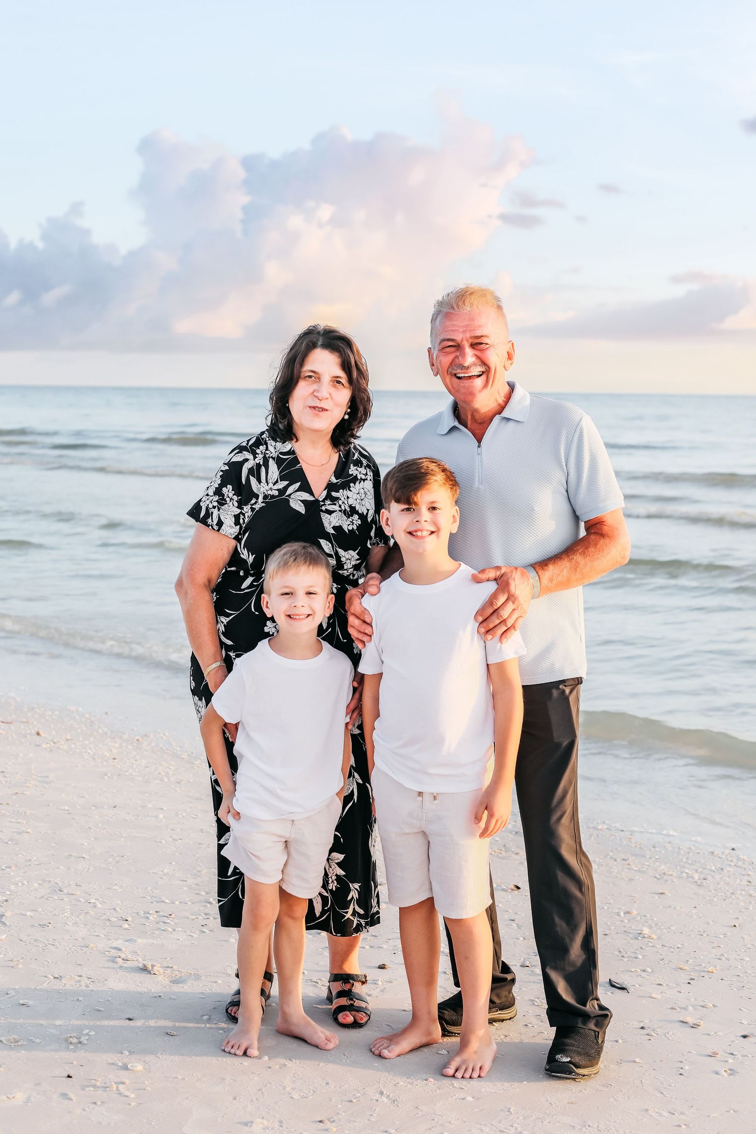 A family poses together on a sandy beach at sunset with ocean waves in the background.