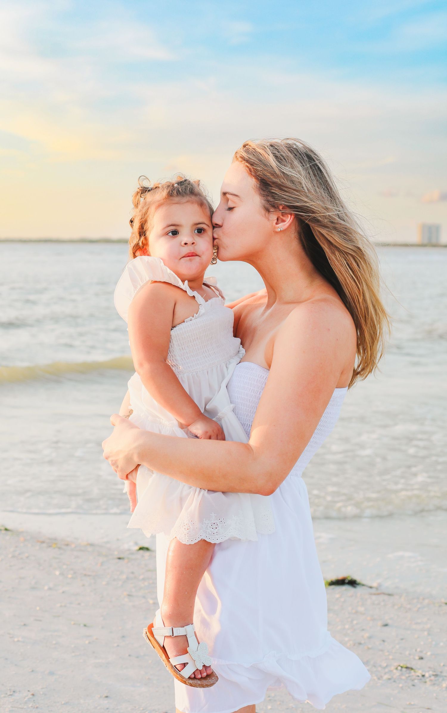 Sweet beach moment between mother and child in matching white dresses.