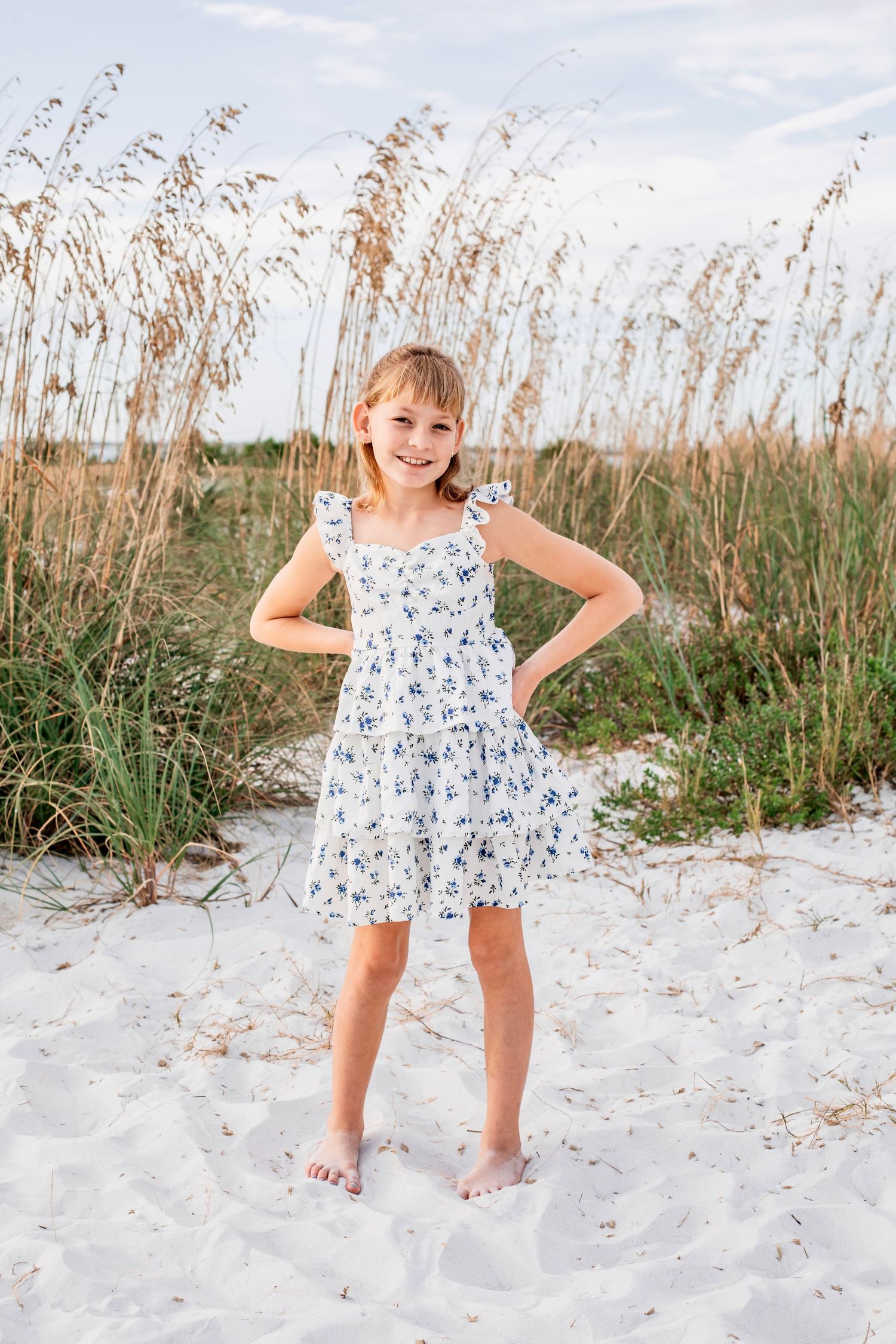 A series of playful beach photos showing a child in a floral dress playing and posing in white sand.