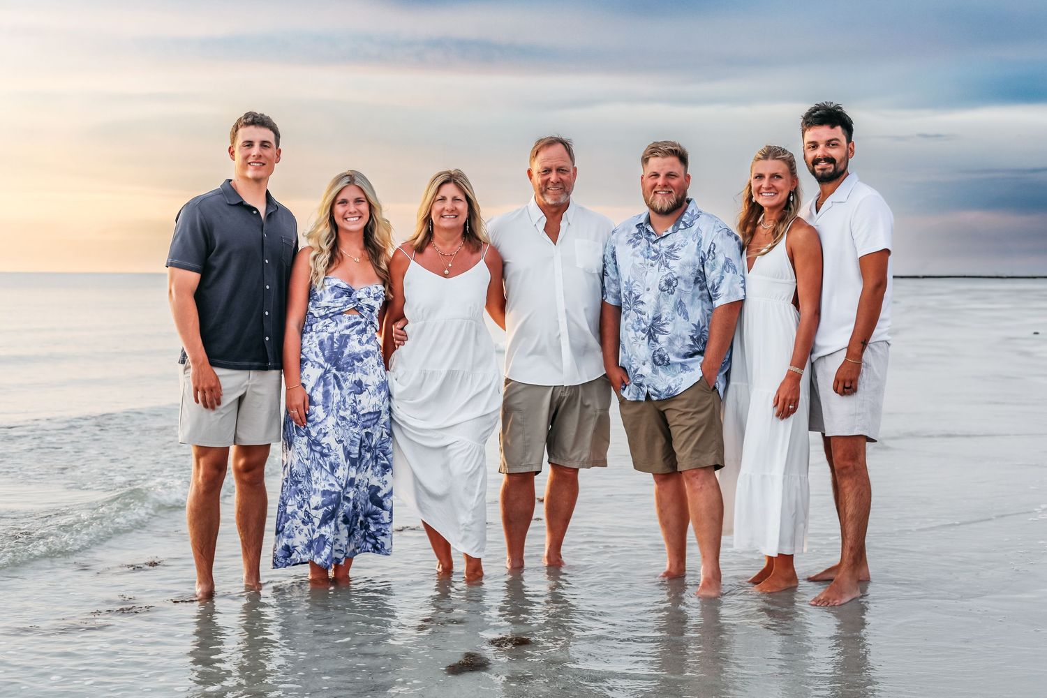 A group stands together along the shoreline at sunset wearing casual beach attire in blue and white.