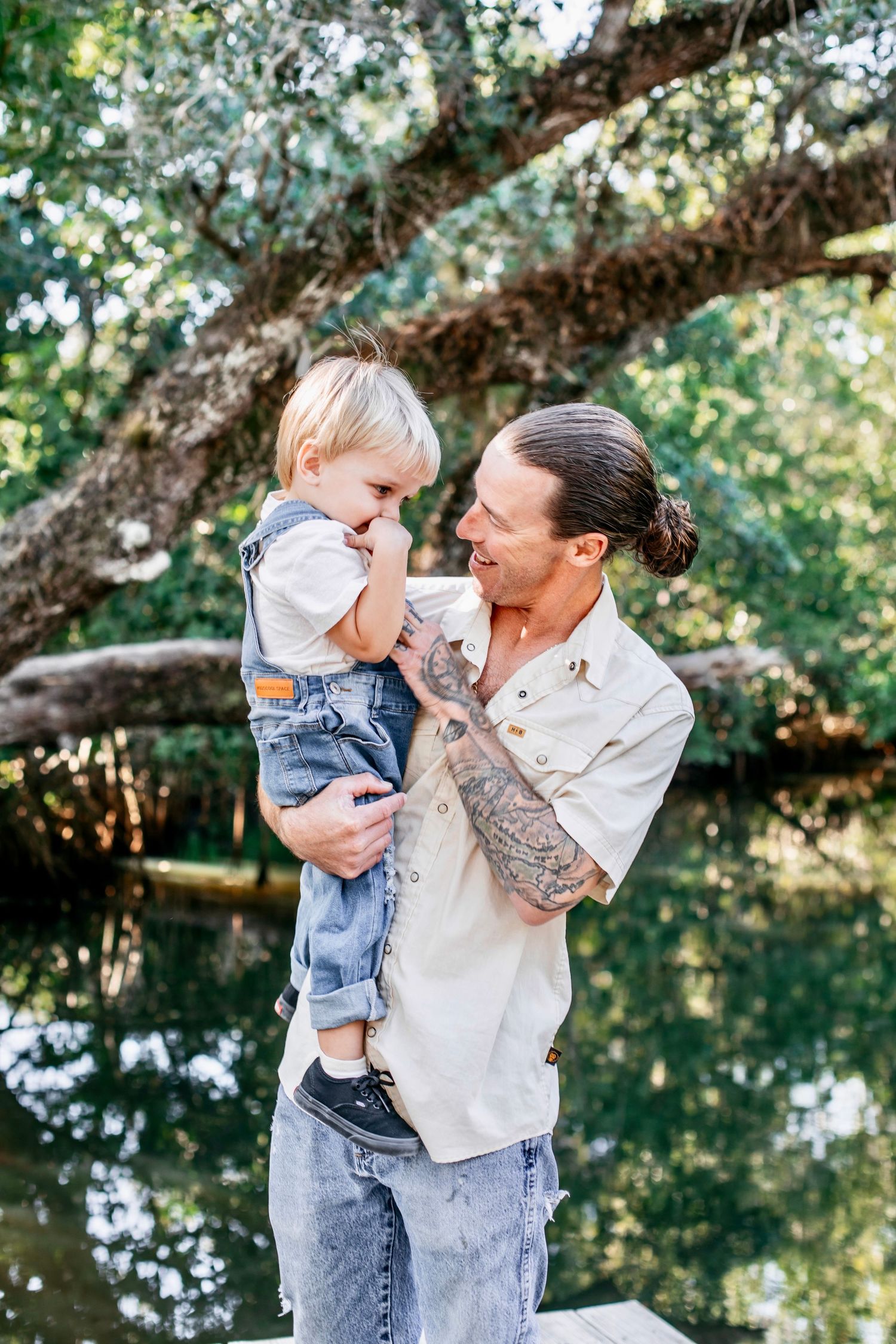 Parent and toddler share joyful moments outdoors near a tranquil pond on a sunny afternoon.