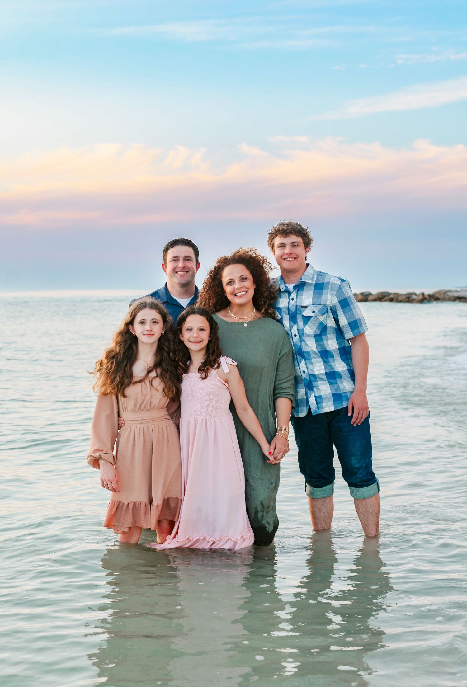 Group standing together in shallow ocean water during sunset photoshoot.