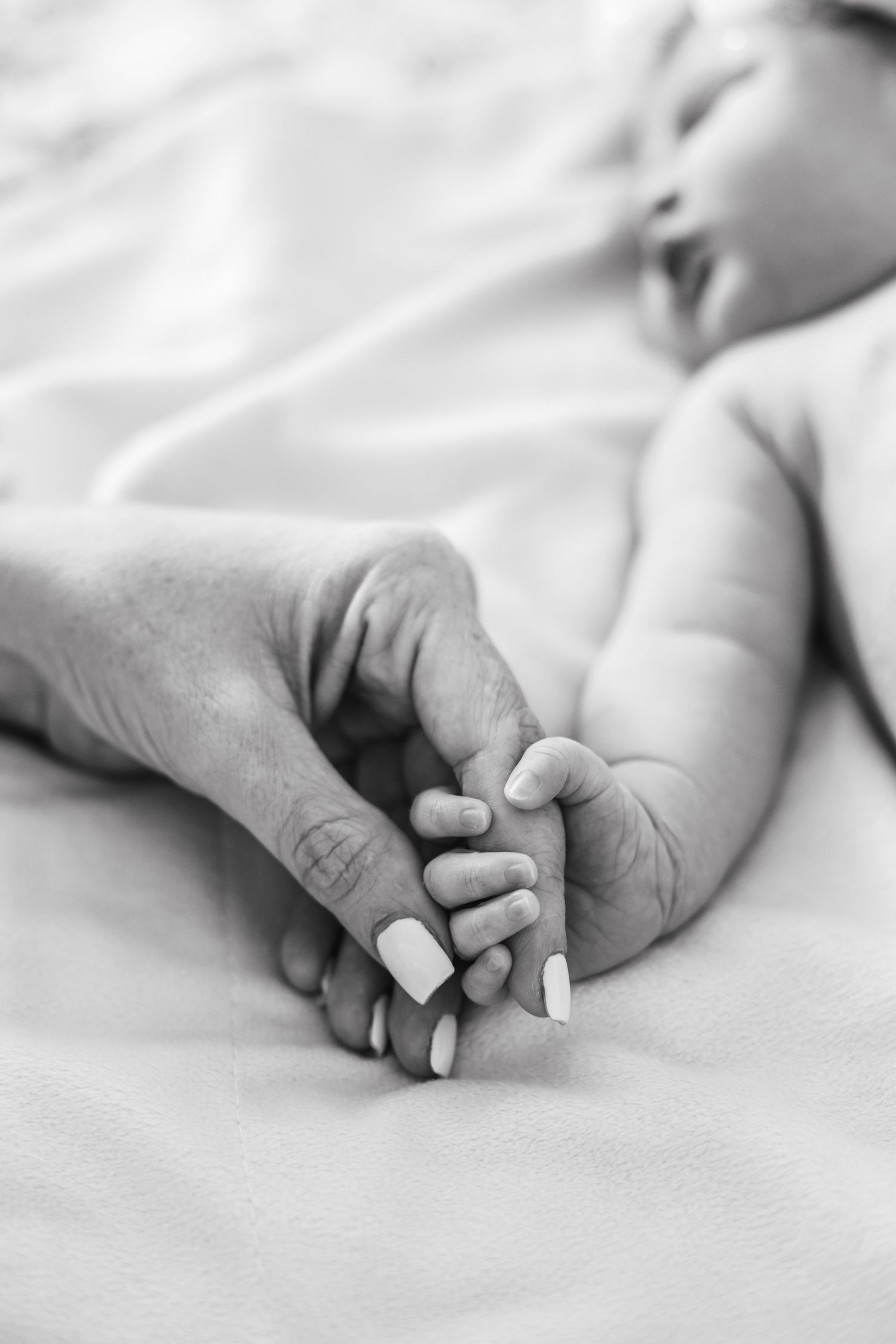 Close-up black and white photo of baby feet holding an adult's finger.