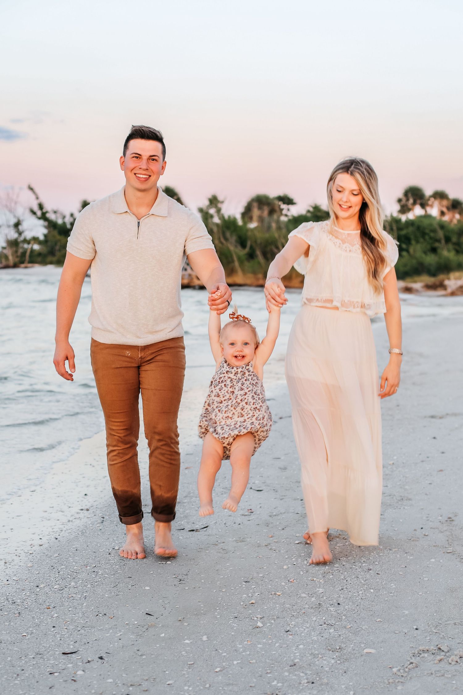 Family walking together on a sandy beach at sunset wearing coordinated cream and brown outfits.