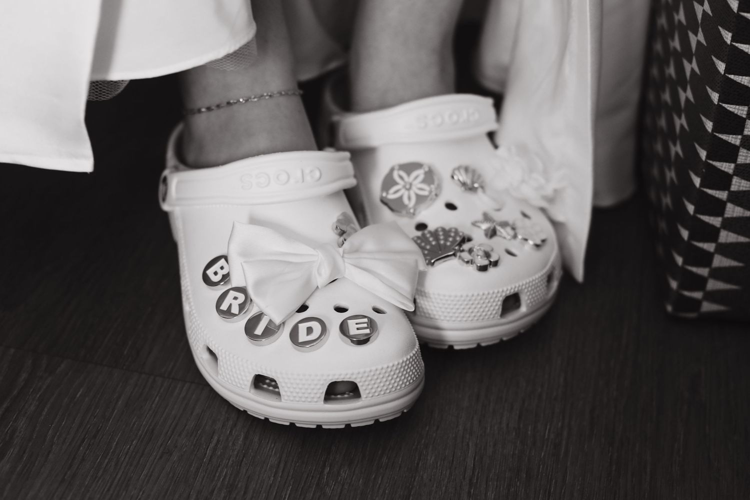 Black and white photo of white Crocs wedding shoes with BRIDE letter charms and decorative jibbitz on a bride.