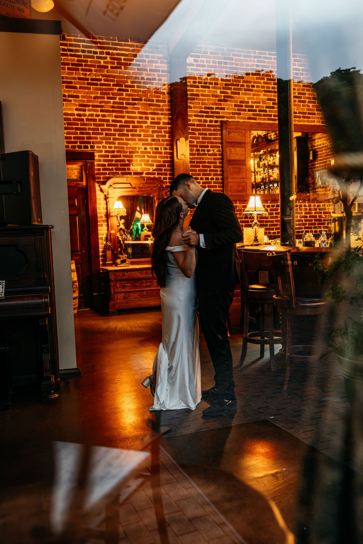 Couple sharing a romantic first dance in a warmly lit venue with exposed brick walls and wooden floors.