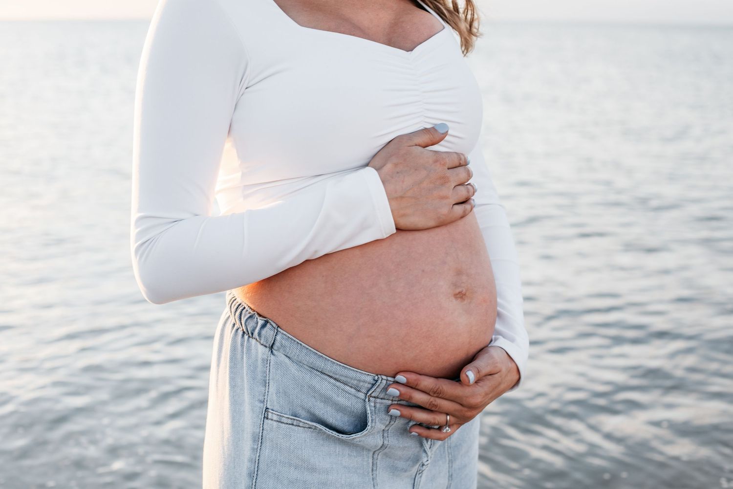 A couple embraces during a romantic maternity photoshoot at the beach during sunset.