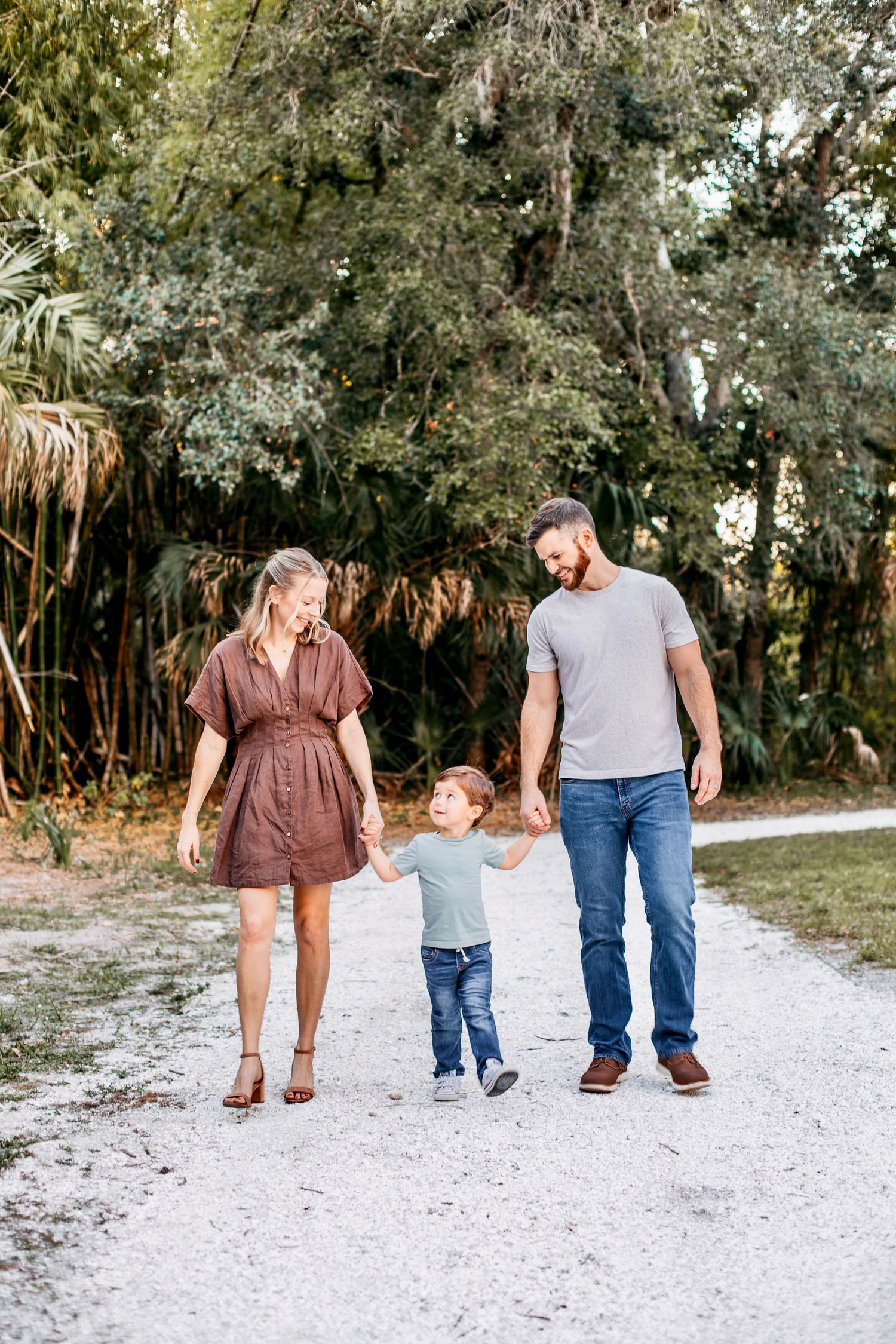 Family walking together on white sandy path through lush green trees in Florida.