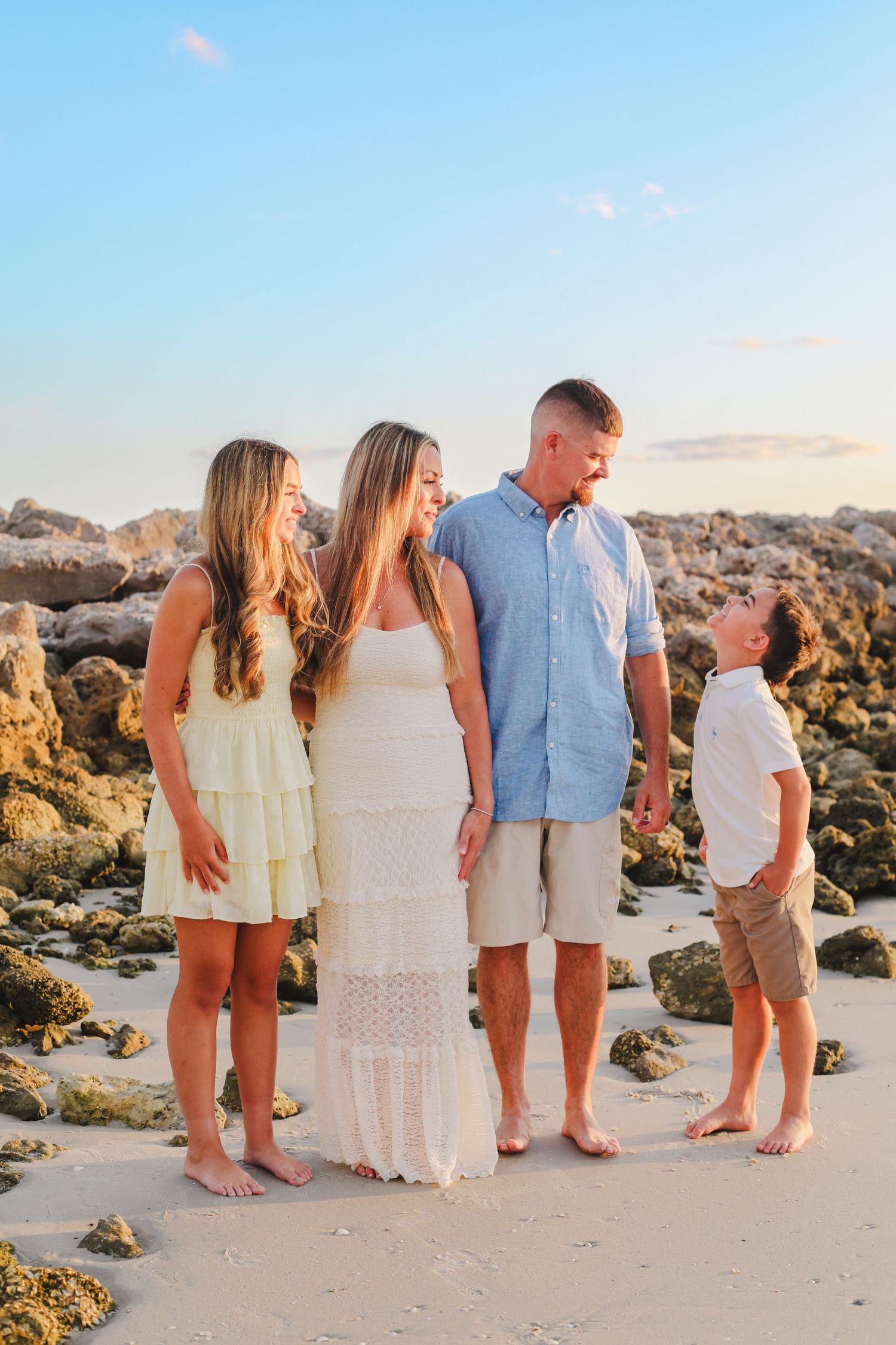 Group portrait on sandy beach with rocky outcrops during golden hour.