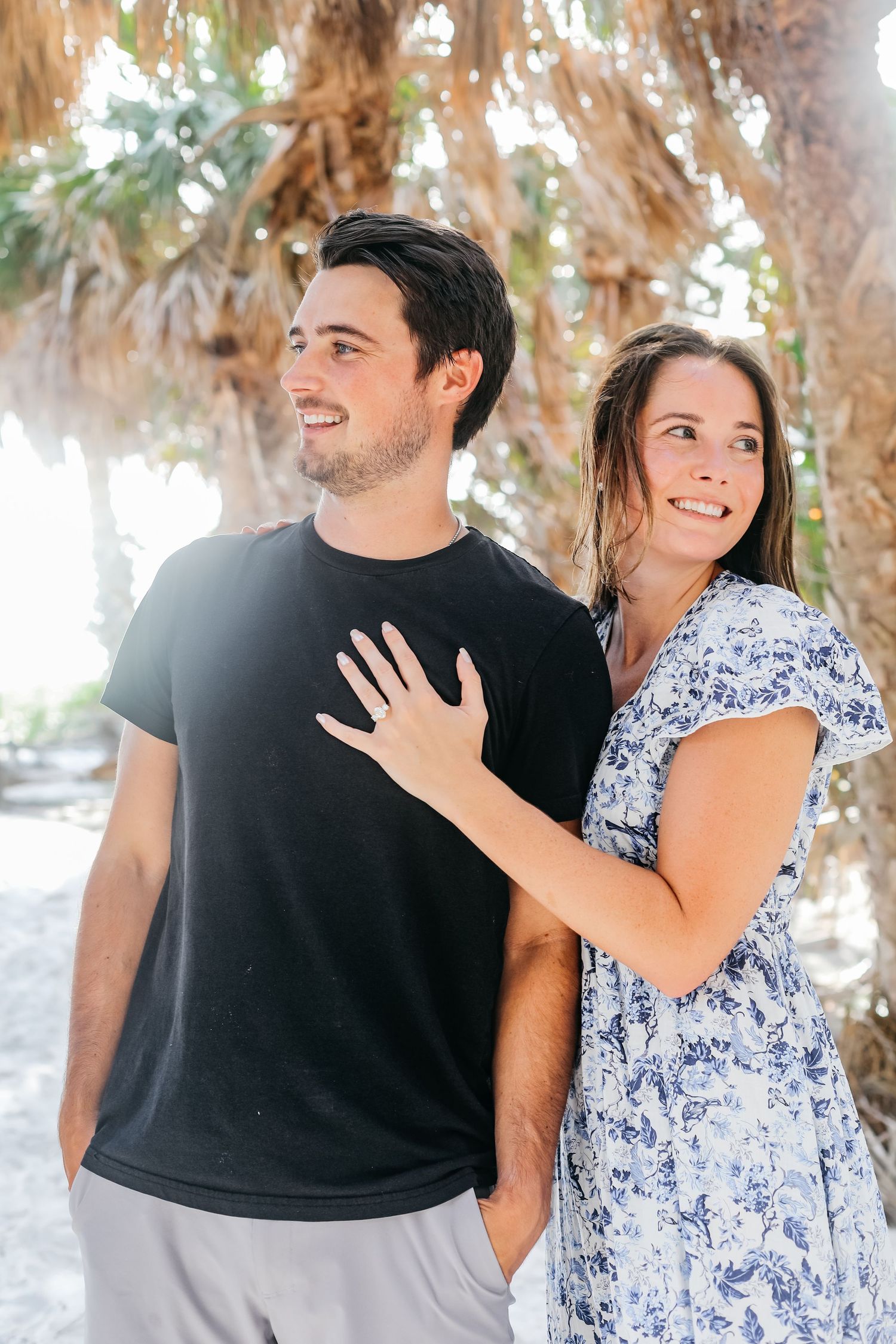 Couple sharing joyful moments on palm-lined beach in casual attire.
