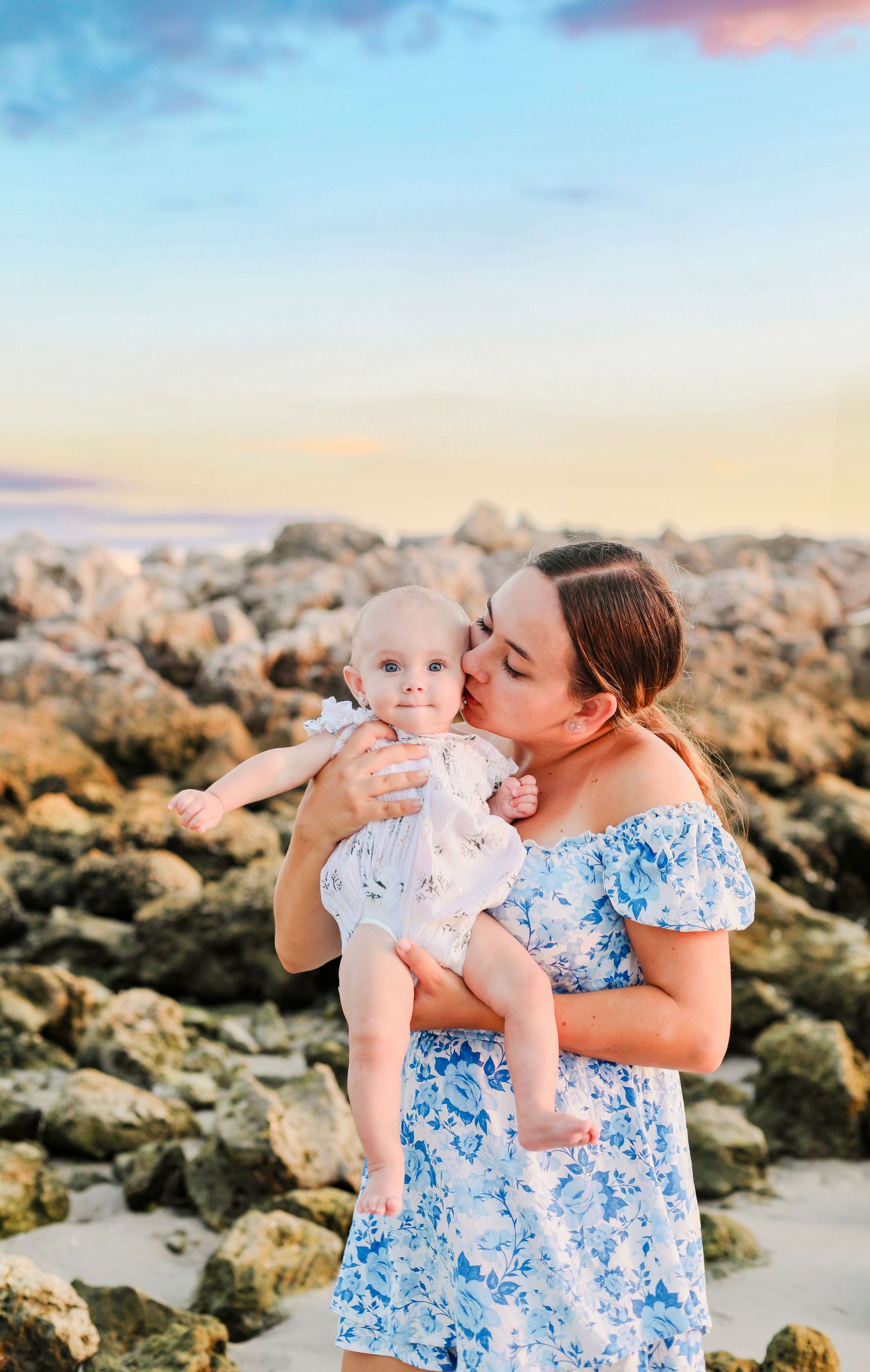 Mother and baby photographed against rocky coastal backdrop during sunset.