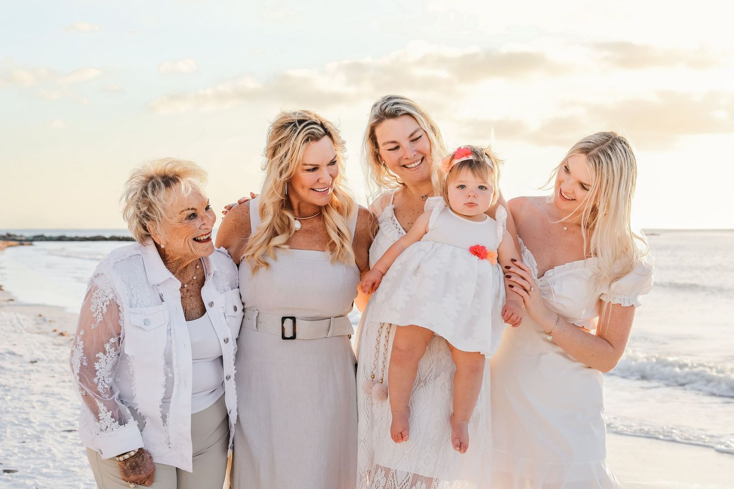 A group in white outfits poses together on a sunny beach for a family photo session.